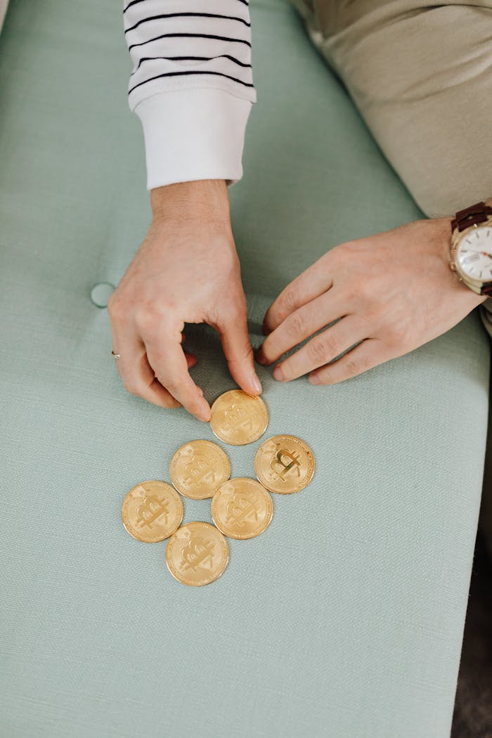 Close-up of hands arranging gold bitcoins on a green surface. Striped sleeves visible.